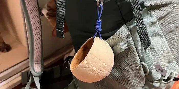 Handcrafted coconut shell outdoor cup clipped to a backpack
