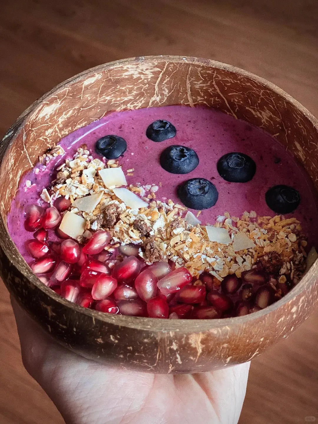 OakenArk coconut bowl filled with açaí, pomegranate seeds, blueberries, granola, and toasted coconut flakes