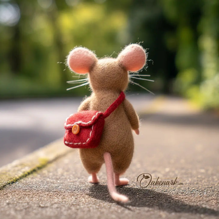Felt mouse with a red bag standing on a road with a blurred green background
