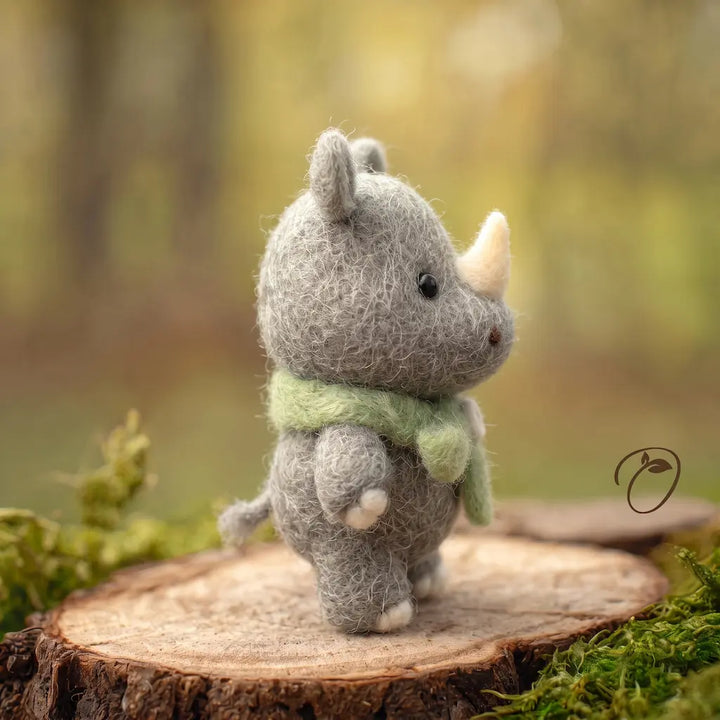 Side view of a gray felt rhino wearing a green scarf, showing its rounded muzzle, cream horn and short tufted tail.