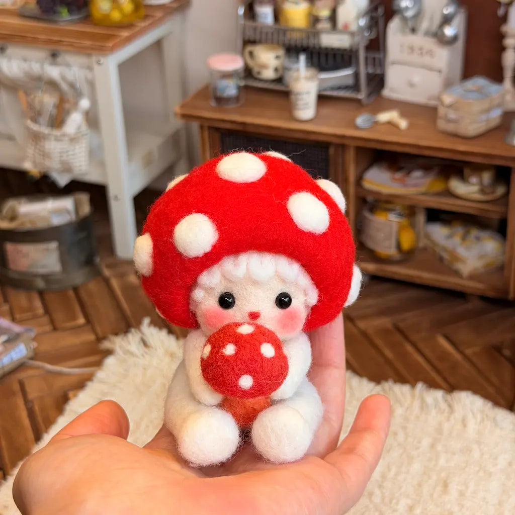 A small felt plush ornament with a red mushroom cap, white polka dots, and a white body is being held in a person&