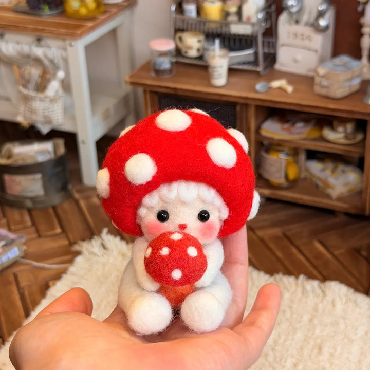A small felt plush ornament with a red mushroom cap, white polka dots, and a white body is being held in a person&