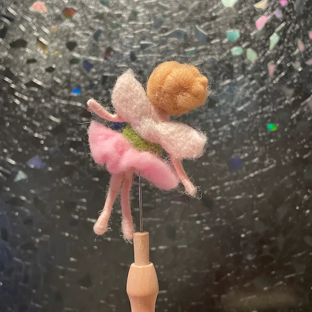 Felted fairy figurine on a wooden stick against a textured black background