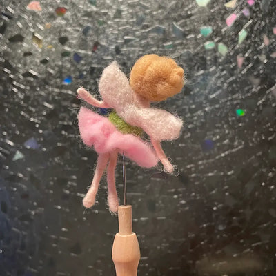 Felted fairy figurine on a wooden stick against a textured black background