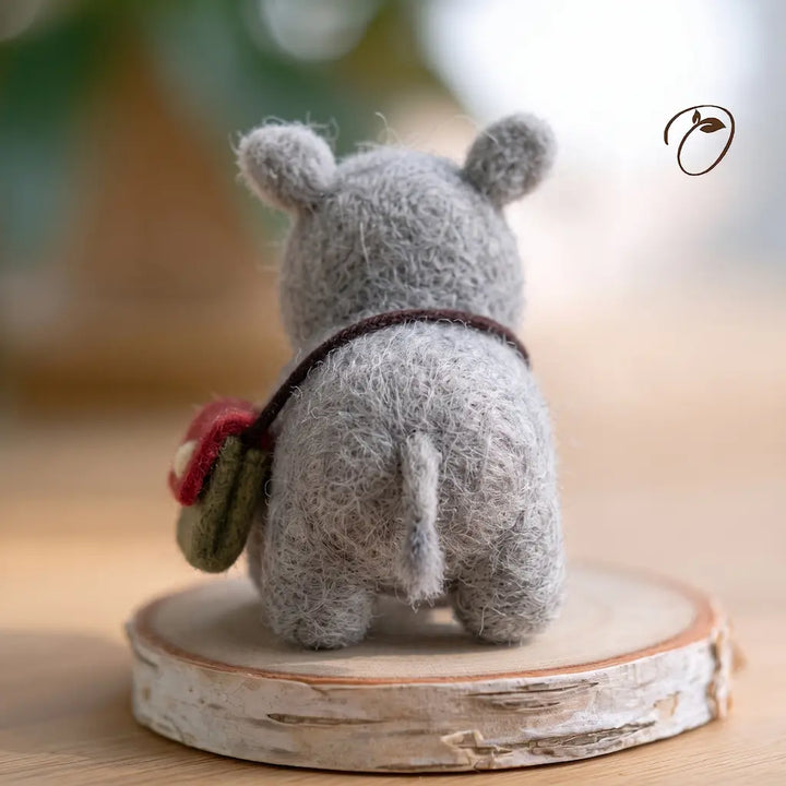 Back view of a gray wool felt rhino showing rounded ears, a slender tail and a dark satchel strap across its back.