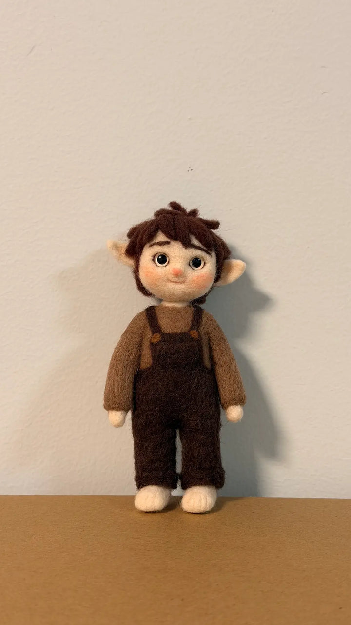 Stuffed toy with brown hair, brown sweater, and overalls on a beige background