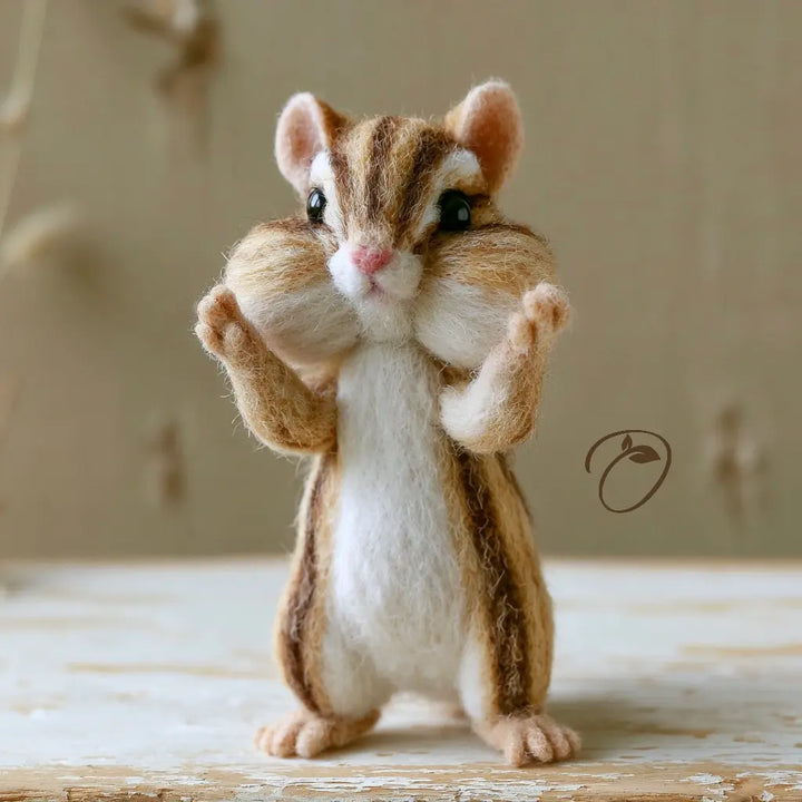 A needle-felted chipmunk figurine standing on its hind legs with its paws raised, set against a soft beige background.