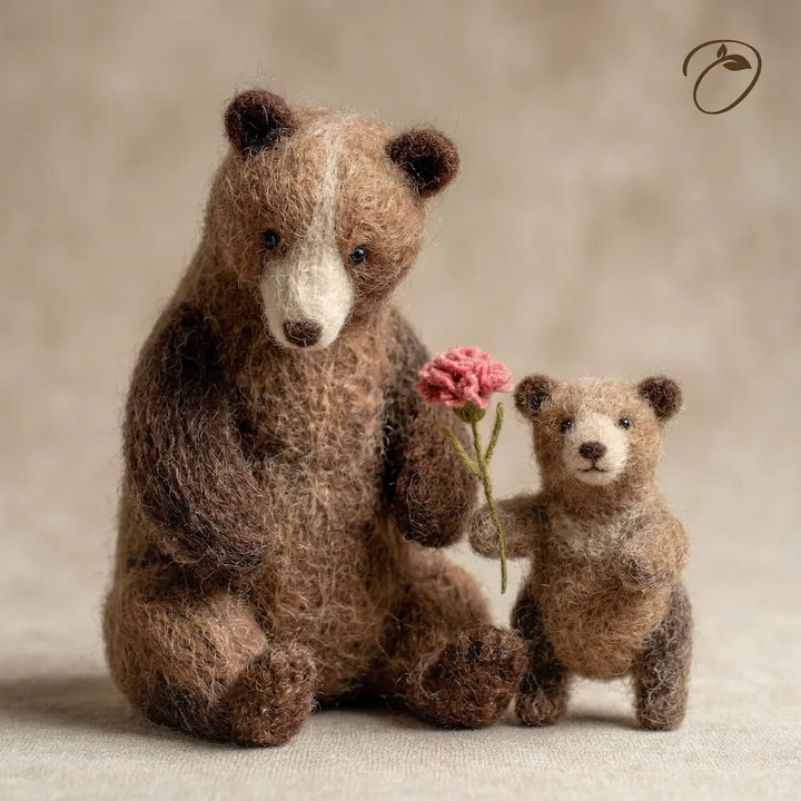 Two needle-felted bears, one holding a pink flower, on a neutral background.
