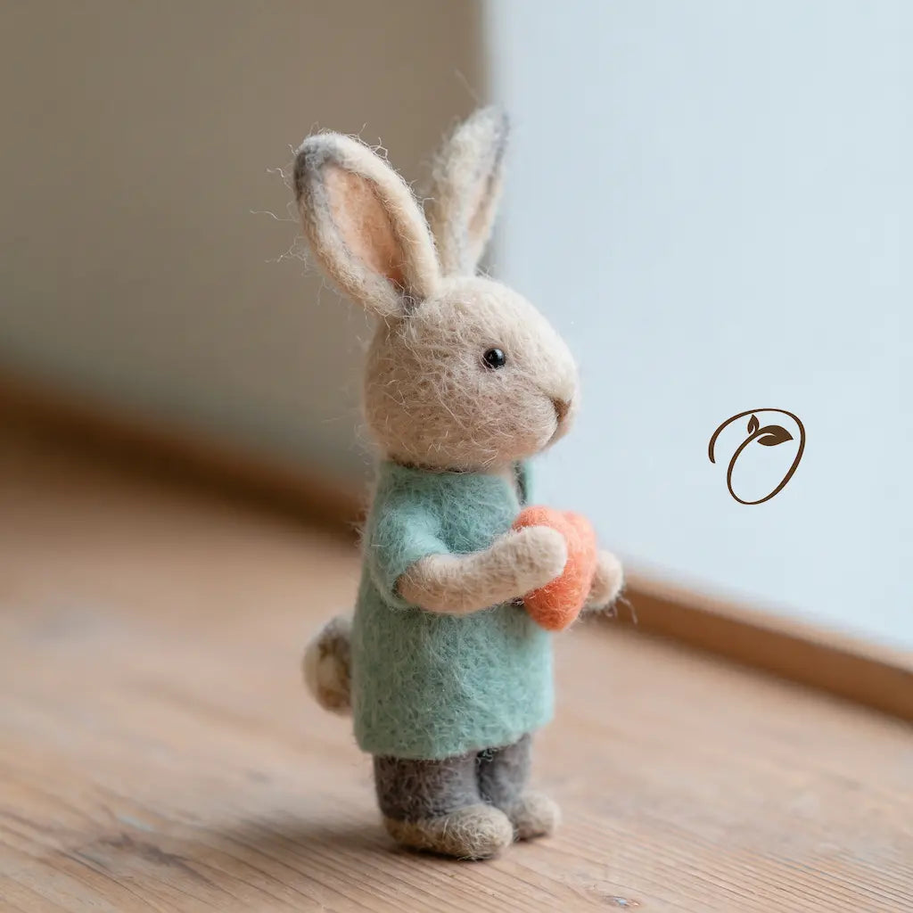 Side view of a wool felt nurse rabbit holding a coral heart, showing its mint uniform top, rounded cheek, upright ears, and small tail.