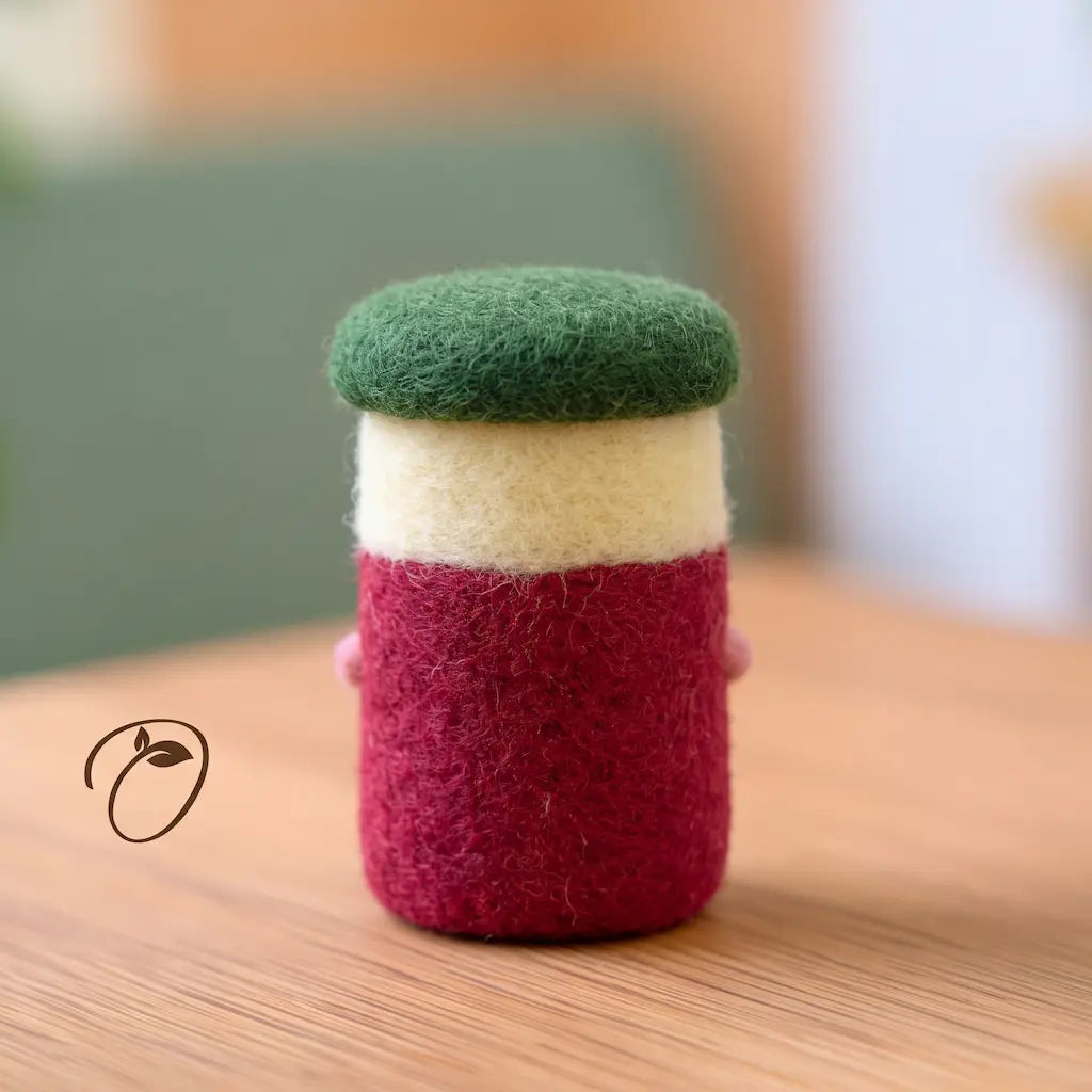 Back view of a cranberry jar felt figurine with a deep red body, cream band, rounded green lid, and visible wool fibers.