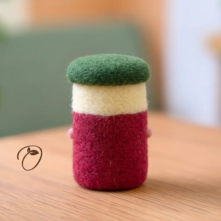 Back view of a cranberry jar felt figurine with a deep red body, cream band, rounded green lid, and visible wool fibers.