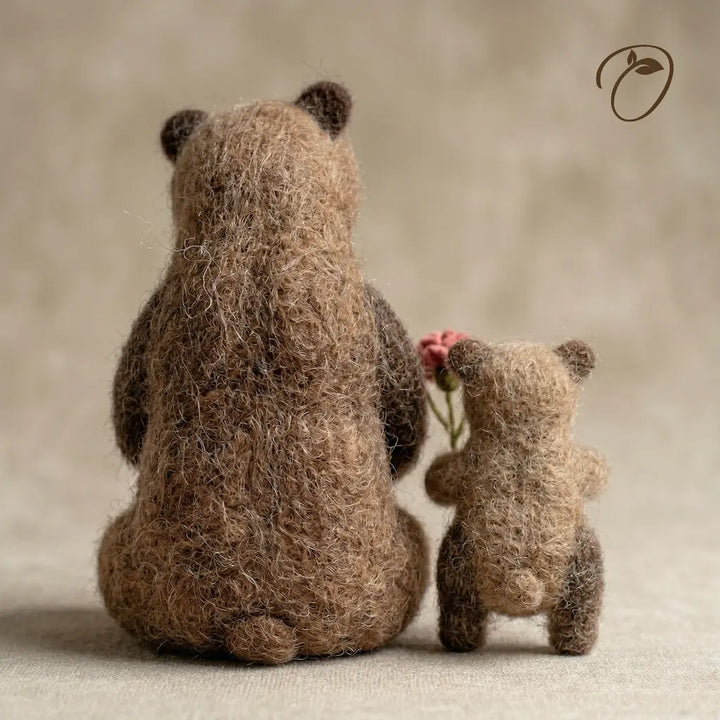 Two brown teddy bears, one holding a pink flower, against a neutral background.