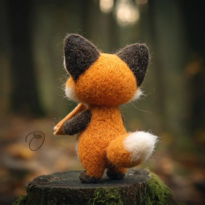 Rear view of an orange wool felt fox showing dark ears, a rounded back, and a curved white-tipped tail.