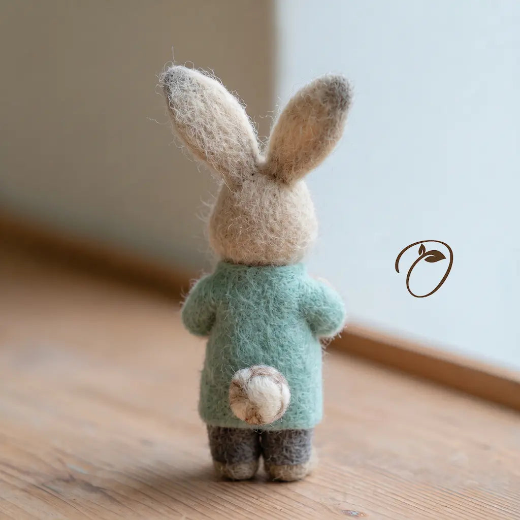 Back view of a felt nurse rabbit with tall ears, a mint uniform top, charcoal-gray trousers, and a round cream-and-brown tail.