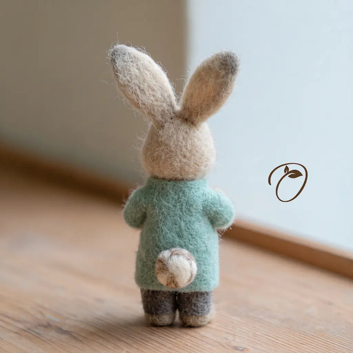 Back view of a felt nurse rabbit with tall ears, a mint uniform top, charcoal-gray trousers, and a round cream-and-brown tail.