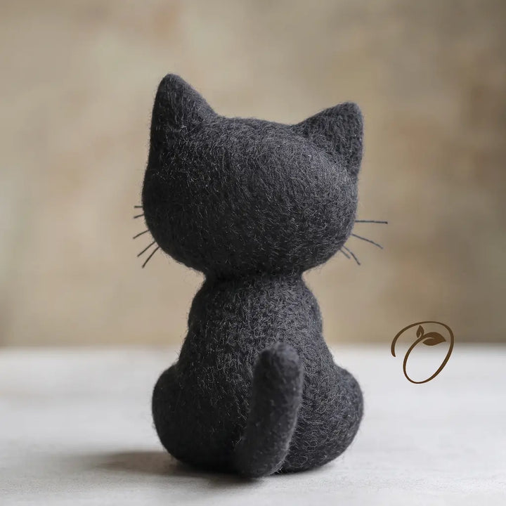 Back view of seated black cat felt figurine showing its rounded head, pointed ears and curved tail