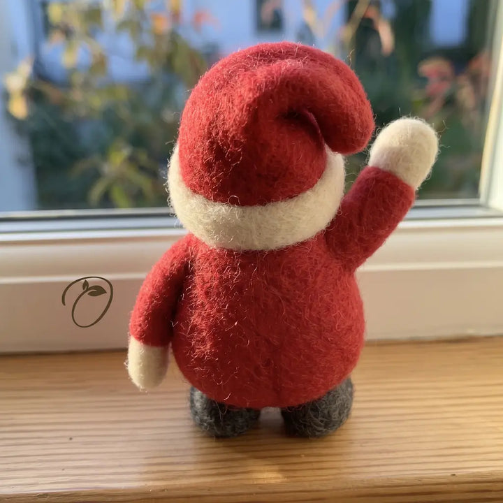 Back view of the waving Santa wool felt figurine with a curved red hat, cream hatband, rounded red coat and gray boots.