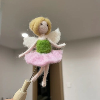 Small fairy figurine with a pink dress and green top on a wooden stick against a neutral background.