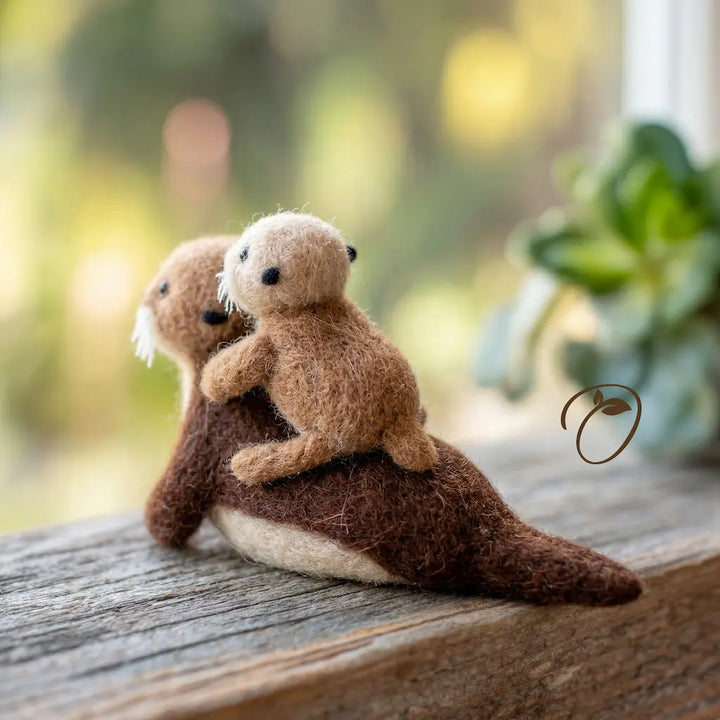 Two plush otters sitting on a wooden surface with a blurred natural background