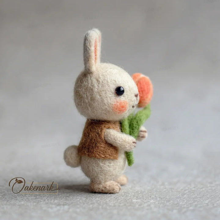 Small felted rabbit toy holding a bouquet of flowers on a neutral background