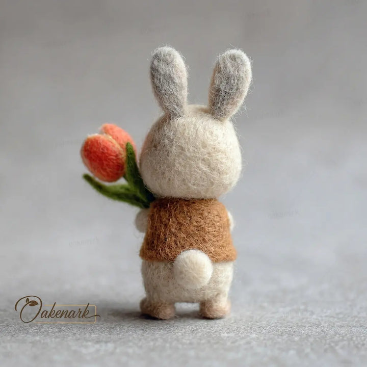 Small felt rabbit toy holding tulips on a neutral background