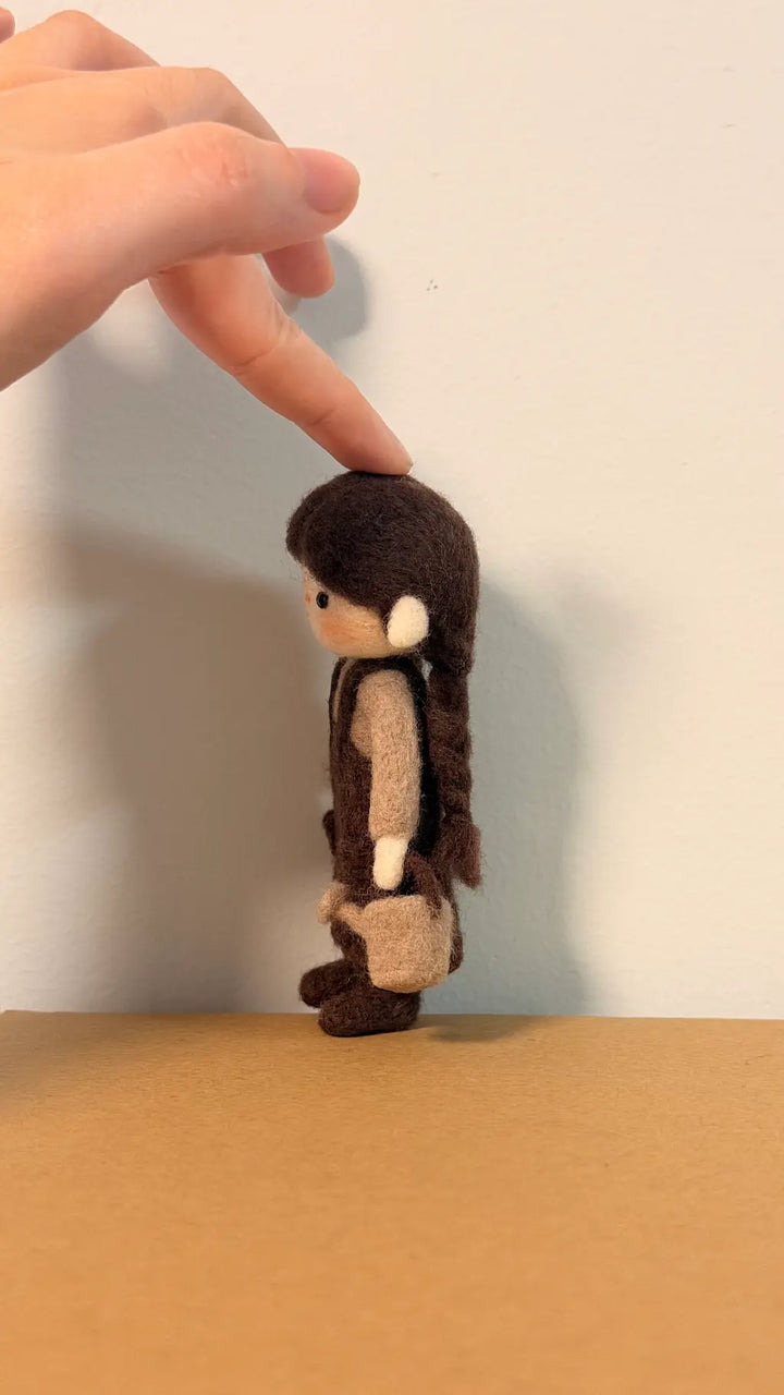 Small brown and beige figurine held by a hand against a plain background
