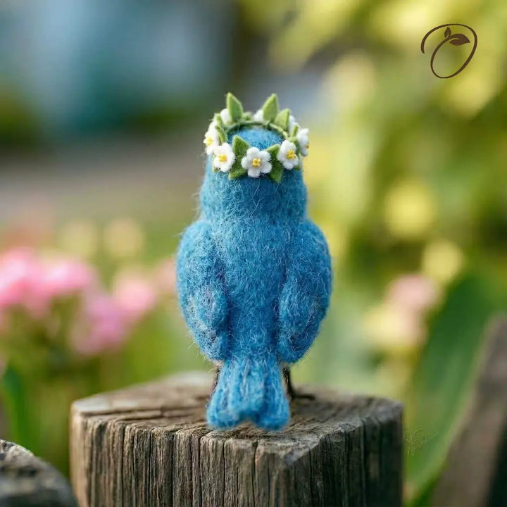 Blue felted bird with a floral crown on a wooden post with a blurred natural background