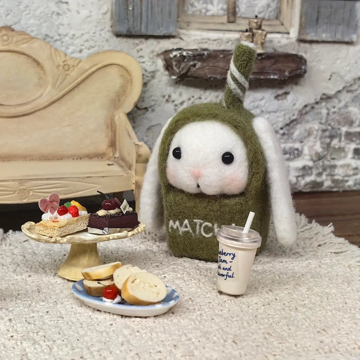 Matcha Bunny felt figurine with miniature cakes, bread and drink in a cozy cafe display