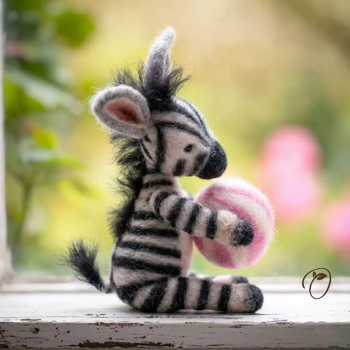 Stuffed zebra toy holding a pink heart with a blurred natural background