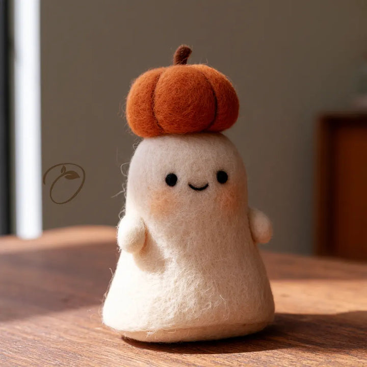 Ivory wool felt ghost with a smiling face, rosy cheeks, and an orange pumpkin crown, viewed from the front.