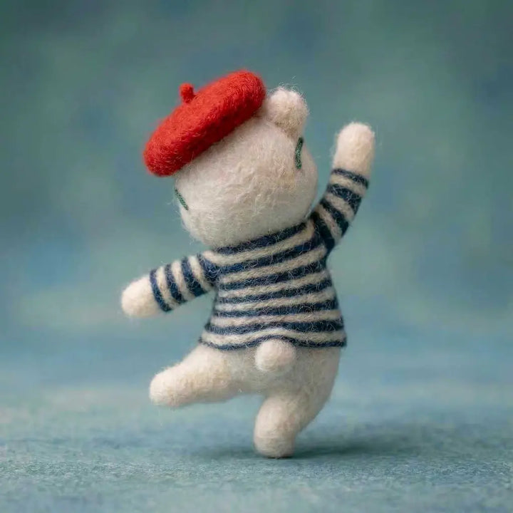 Small plush toy resembling a cat wearing a red beret and striped sweater on a blue background