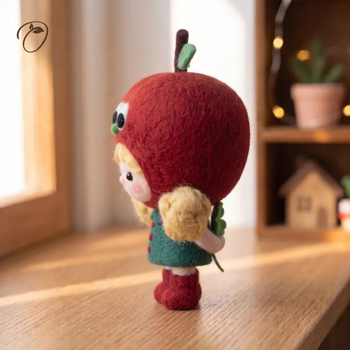Back view of a wool felt apple girl holding a green clover behind her back, with blonde pigtails and red boots.
