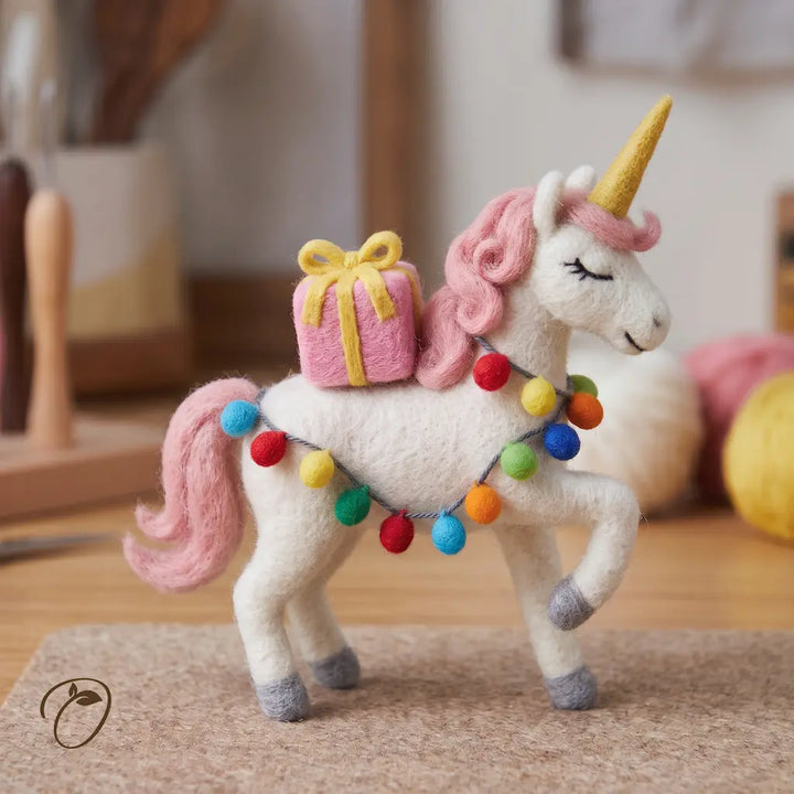 Right-facing white felt unicorn with a pink mane, yellow horn, pink present and colorful felt ball garland.