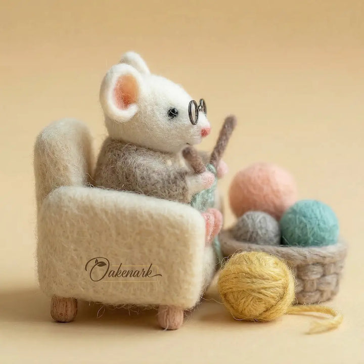White mouse toy with glasses sitting on a chair next to yarn balls, on a beige background.
