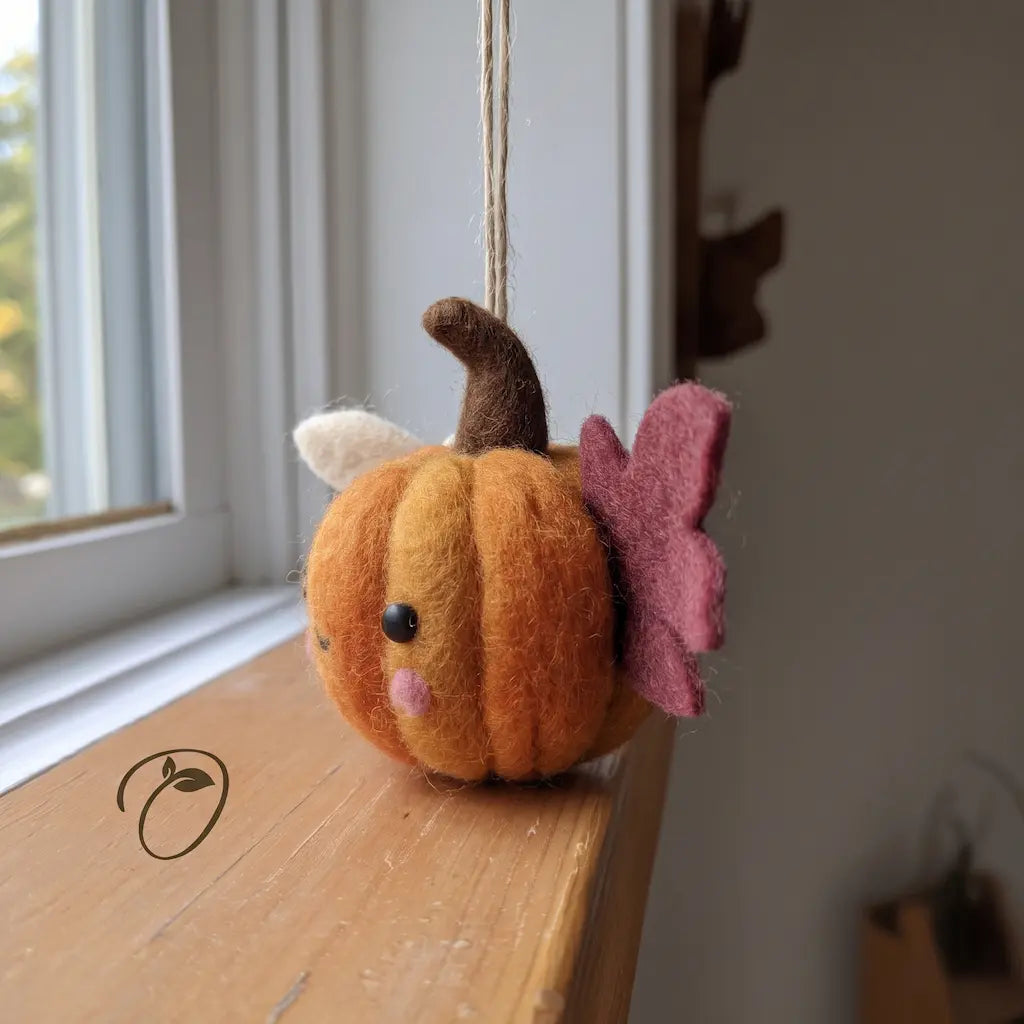 Side view of a winged felt pumpkin showing rounded orange segments, a cranberry-colored wing, a rosy cheek, and a hanging cord.