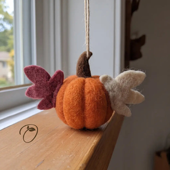 Back view of an orange wool felt pumpkin ornament with ivory and cranberry wings, sculpted segments, and a brown stem beneath the hanging cord.