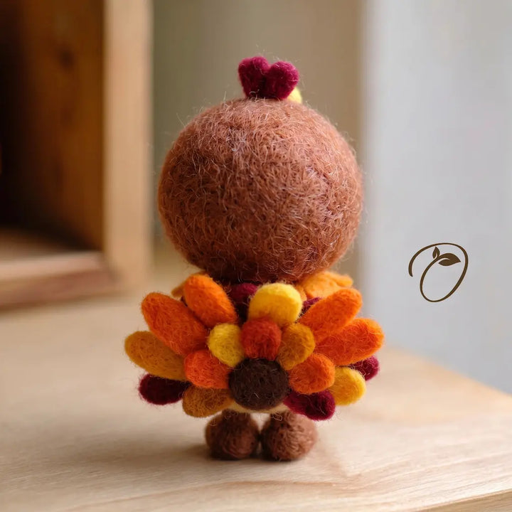 Back view of a handmade felt turkey sprite with a rounded brown hood and a fan of orange, yellow, and cranberry-colored feathers.