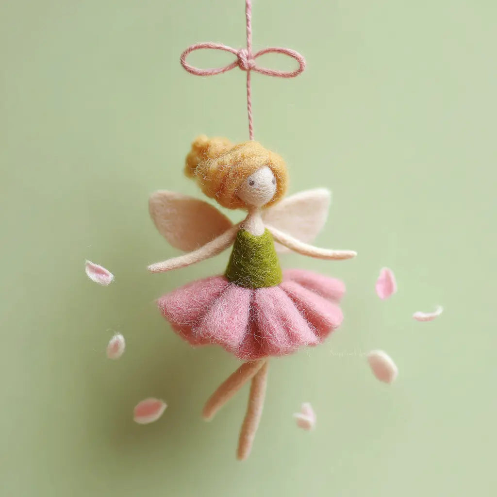 Felt fairy doll with pink skirt and green top hanging against a light green background with pink petals.
