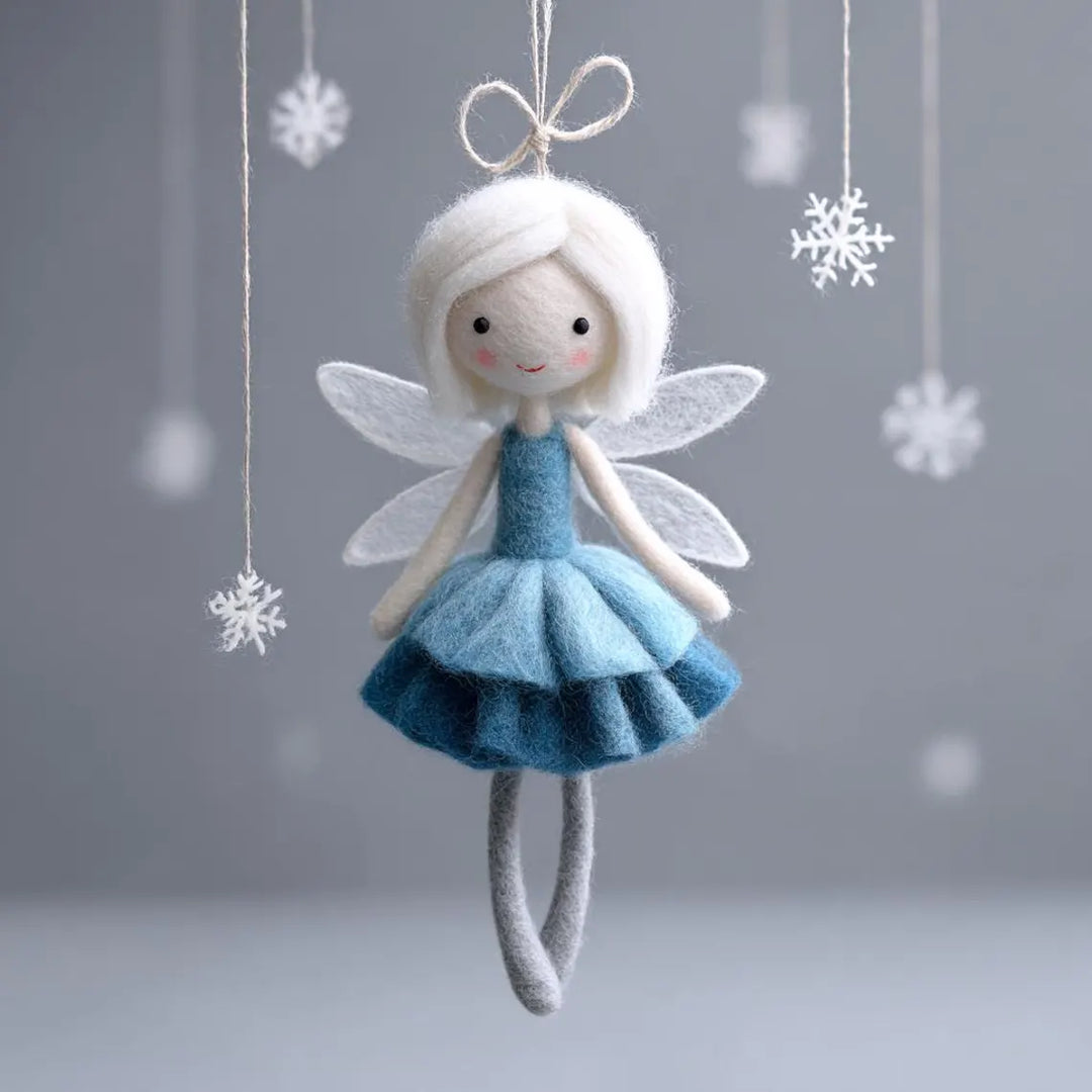 Felt fairy doll with blue dress and white wings hanging against a gray background with snowflake decorations.