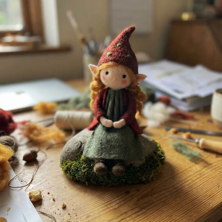 Felted gnome figurine on a wooden surface with crafting materials in the background