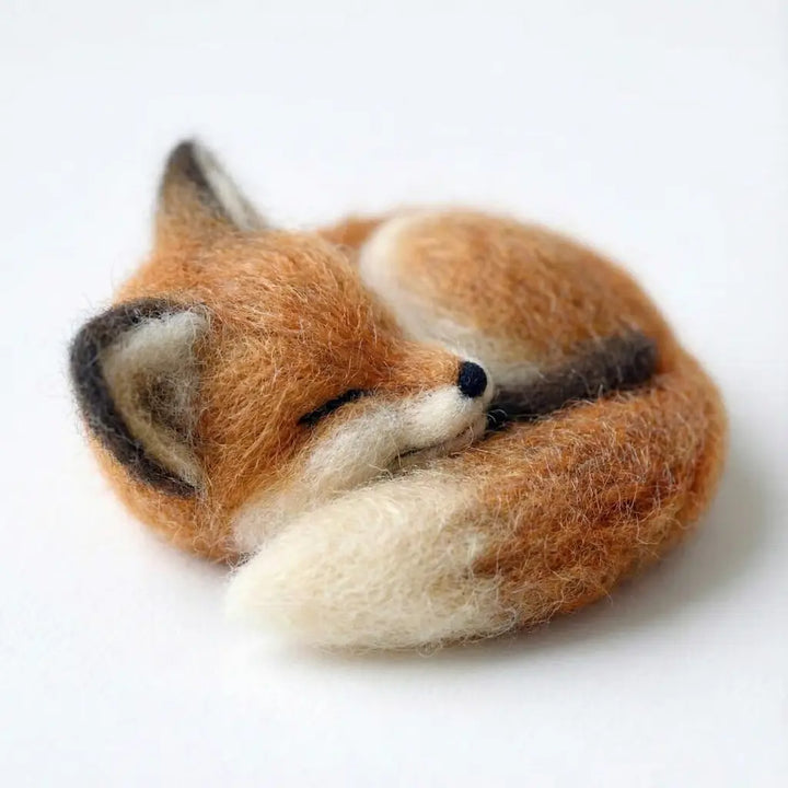 Felted fox toy sleeping on a white background