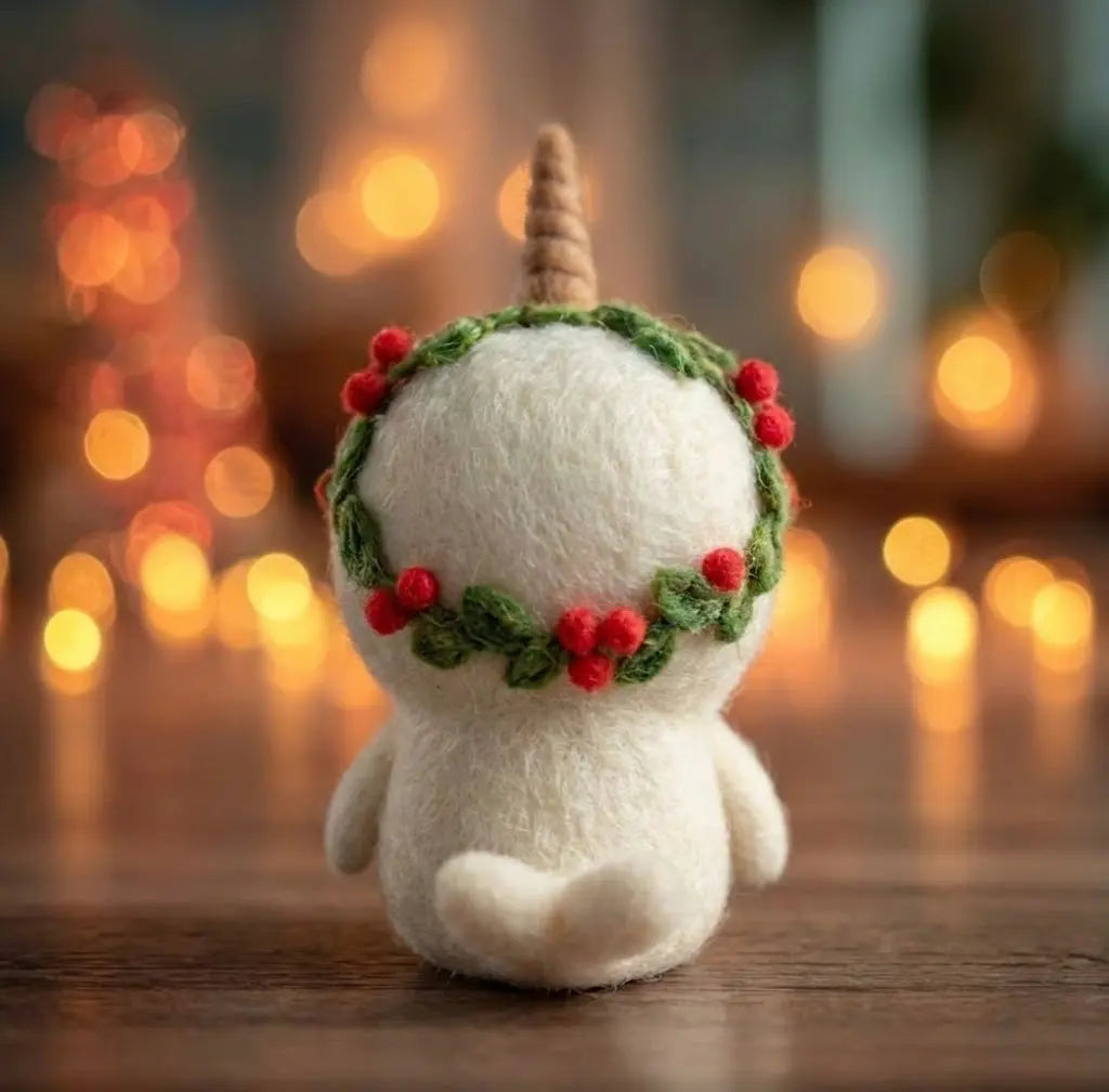 White plush toy with a unicorn horn and berry wreath on a wooden surface with blurred lights in the background