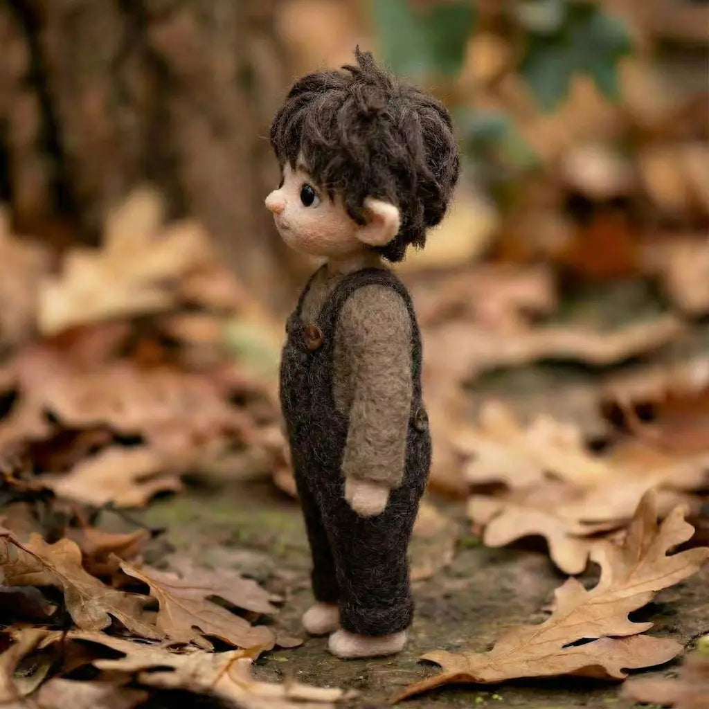 Small figurine of a boy in overalls standing on a leaf-covered ground with blurred natural background
