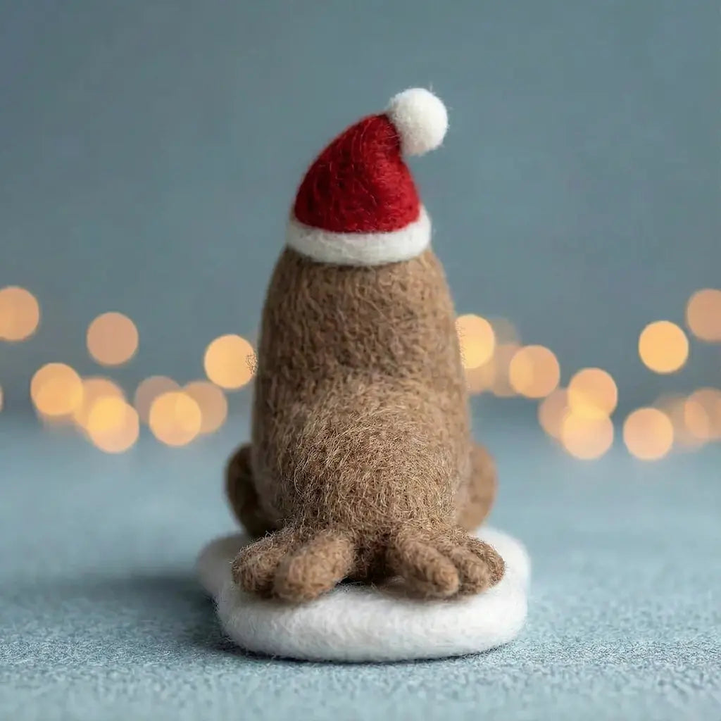Small brown dog figurine wearing a red Santa hat on a light blue background with blurred lights.