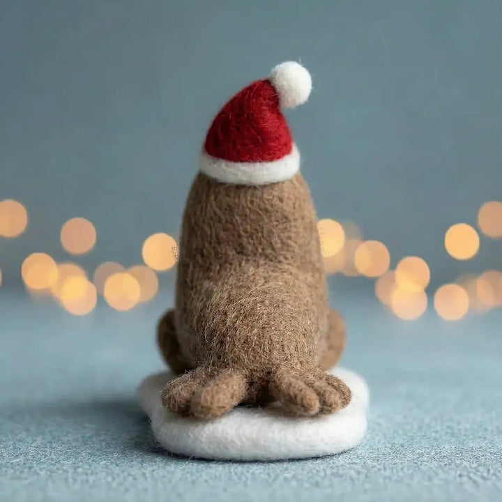 Small brown dog figurine wearing a red Santa hat on a light blue background with blurred lights.