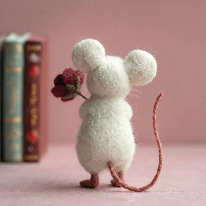 White mouse figurine holding a red flower against a pink background