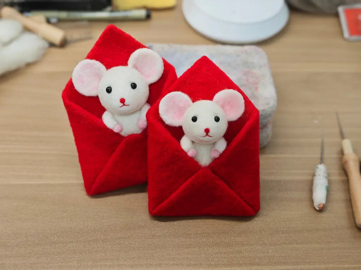 Two red envelopes with plush mouse toys on a wooden surface.