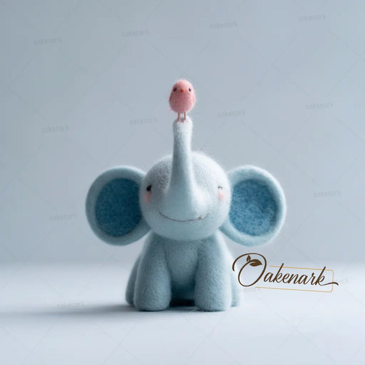 Plush elephant toy with a pink bird on its trunk against a light gray background, featuring the brand &