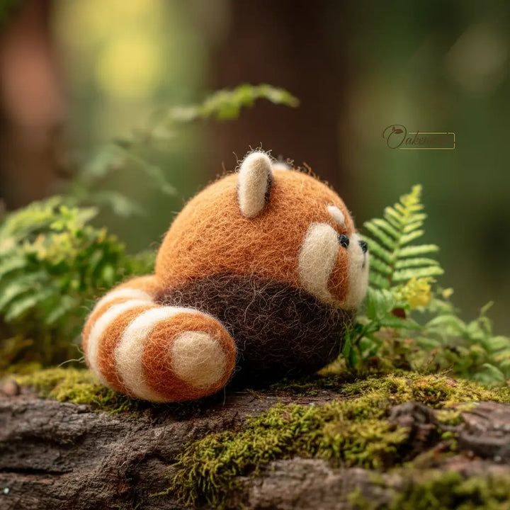 Felt toy red panda on a log with green foliage in the background