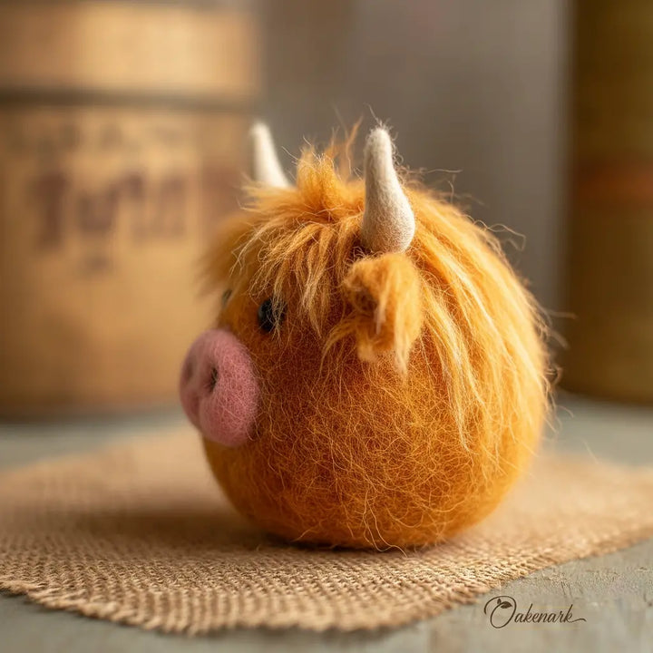 Felted Highland cow on a textured surface with a blurred background